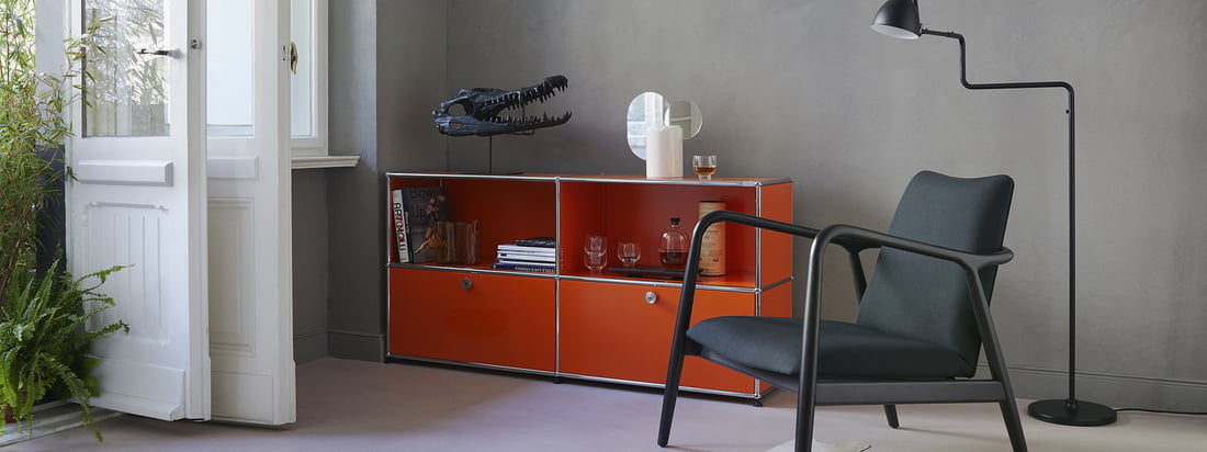 USM Haller - Herstellerserie - Wohnzimmer - Sideboard M - orange - Sessel - Stehleuchte - Bücher - Gläser - weiße Türen - Pflanzen - Ambiente