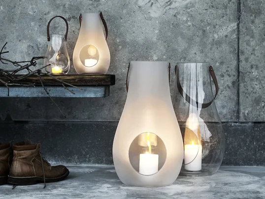 Ein Paradebeispiel für stilvolle und schöne Geschenke für Frauen: die Design with Light Laterne von Holmegaard aus durchsichtigem bzw. matt-weißem Glas und einem Tragegriff aus Leder.