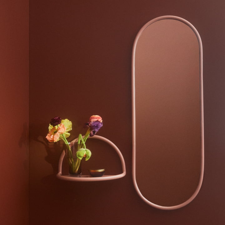 Der Angui Wandspiegel mit rosefarbenem Rahmen von AYTM neben einem kleinen Wandregal in derselben Farbe