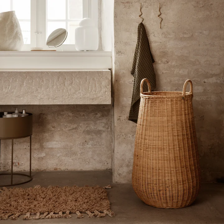 Der Amass Hochflor Fußabtreter von Ferm Living unter dem Waschbecken neben einem Rattan-Korb