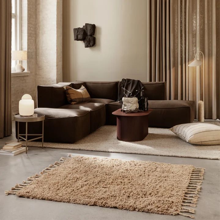 Der Amass Hochflor Teppich von Ferm Living in einem eleganten Wohnzimmer mit braunem Sofa und beigen Vorhängen