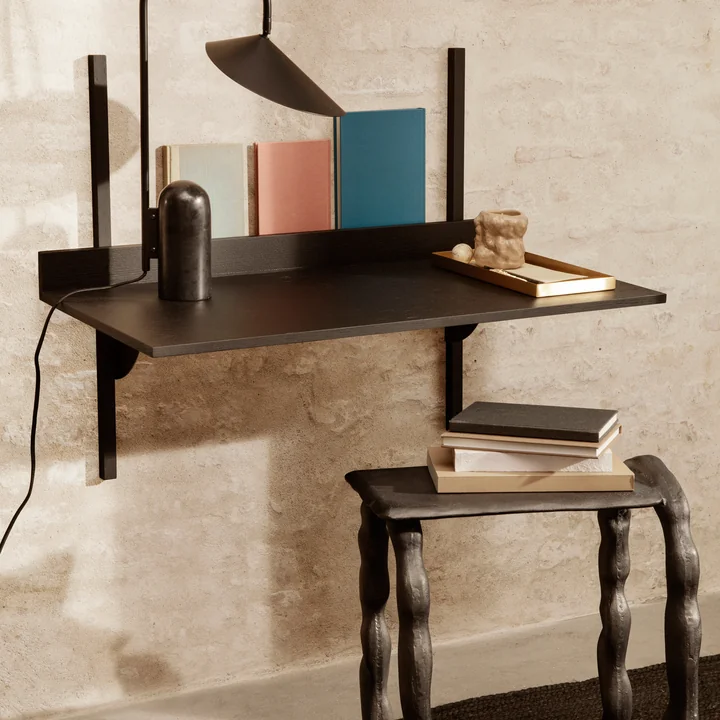 Der Sector Schreibtisch von Ferm Living an der Wand in Kombination mit Büchern, einer Tischleuchte und einem Hocker