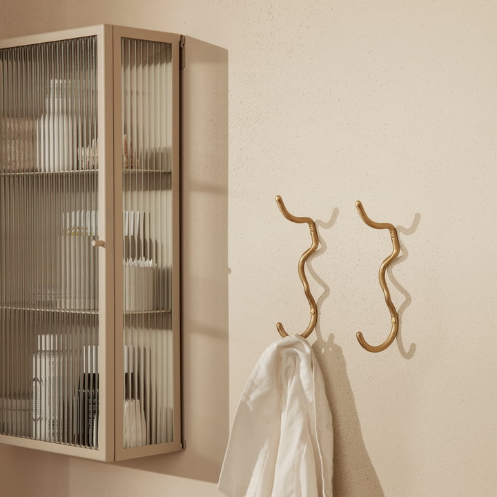 Der Curvature Wandhaken von ferm Living mit einem Handtuch neben einem Wand-Vitrine