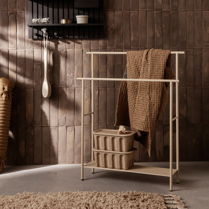 Der Dora Handtuchhalter von Ferm Living mit Handtüchern und Papierboxen neben einem Wandregal