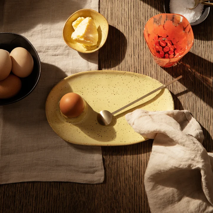 Der gelbe Flow Frühstücksteller von Ferm Living neben Gläsern auf einer beigen Tischdecke