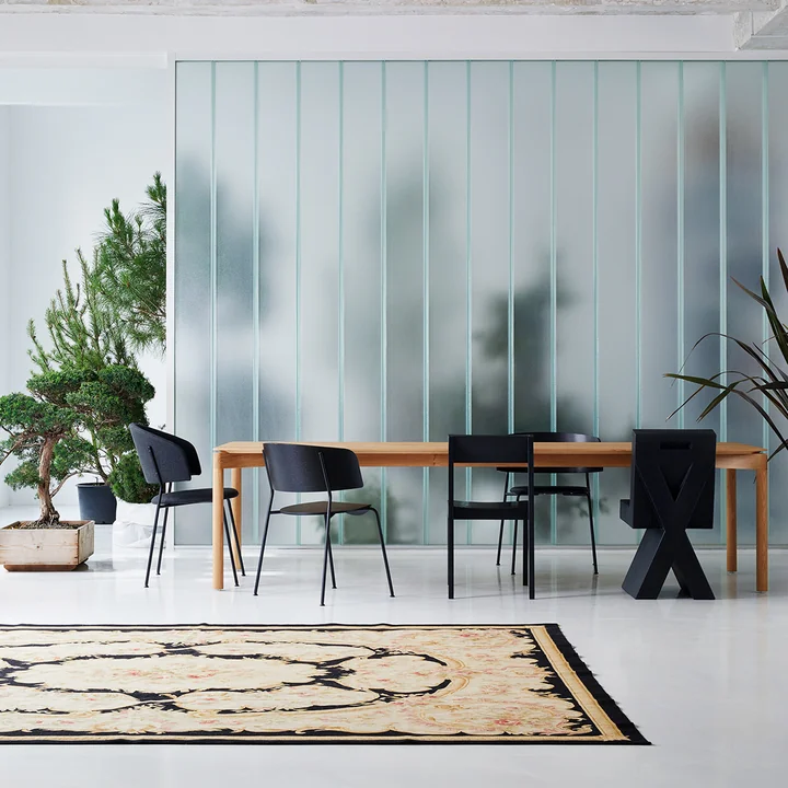 Der Wagner Dining Chair von OUT Objekte unserer Tage in anthrazit an einem großen Holz-Esstisch neben weiteren dunklen Stühlen