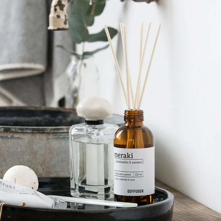 Der Raumduft mit 7 Stäbchen von Meraki auf einem Tablett neben Parfum