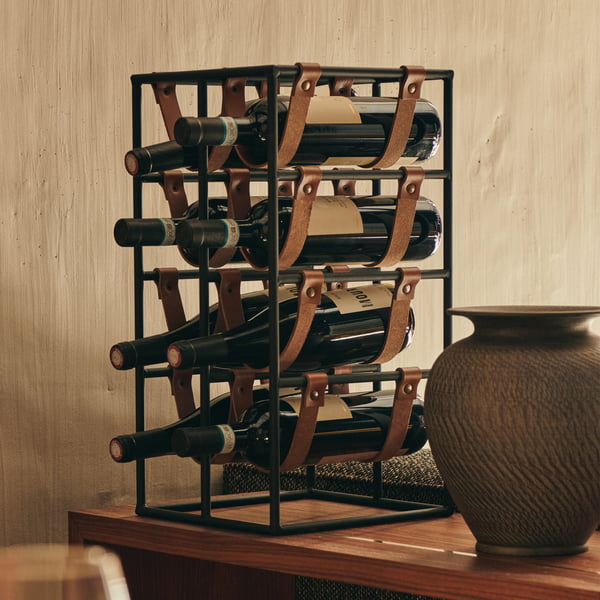 Das Umanoff Weinregal für 8 Flaschen, Stahl schwarz (RAL 9005) / Leder braun von Audo auf einer Holztheke