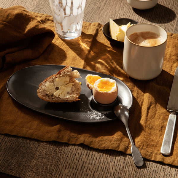 Der Flow Frühstücksteller von ferm Living mit Brot und Ei auf einer braunen Tischdecke 